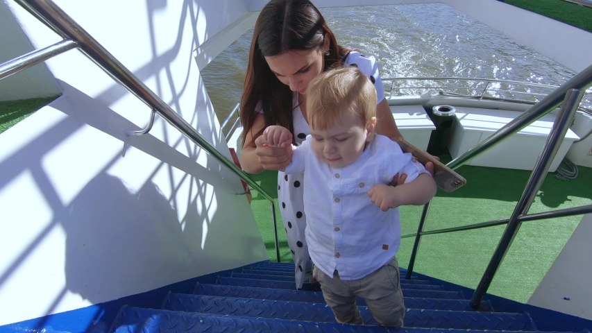 Mom helps baby boy climb the metal stairs of a pleasure craft