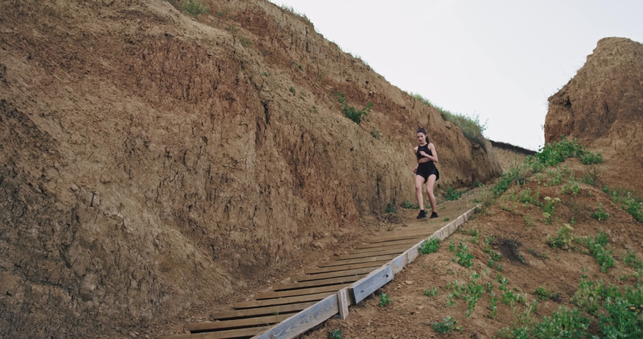 A young athletic woman, runs down  stairs by the mountains