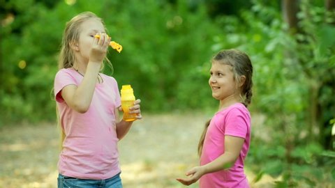 Two little girls blowing bubbles and playing in the Park. Happy childhood concept. Slow motion 120 fps