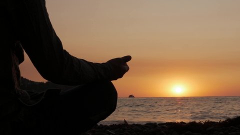Silhouette of a man meditating sitting by the sea at sunrise.