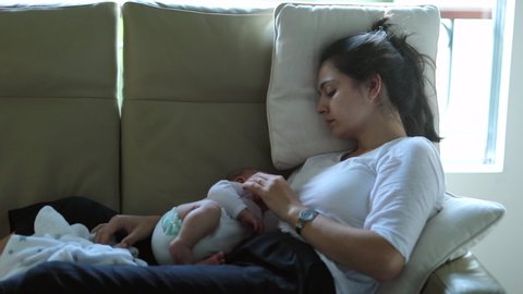 Authentic candid real life tired new mother with newborn baby at home trying to sleep and rest