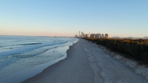 Sun setting on a beach while people walk with the city skyline glistening in the distance