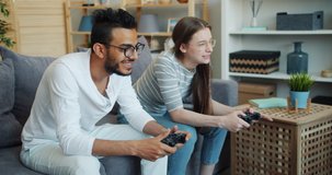 Slow motion of Arabian guy playing video game with cute girlfriend indoors at home having fun sitting on couch together. Hobby, pastime and people concept.