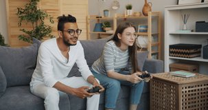 Man and woman happy couple are enjoying video game in apartment having fun together sitting on couch indoors using joysticks. People and lifestyle concept.