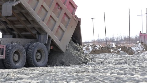 Old rusty dump truck brought frozen earth to winter construction site, unloading