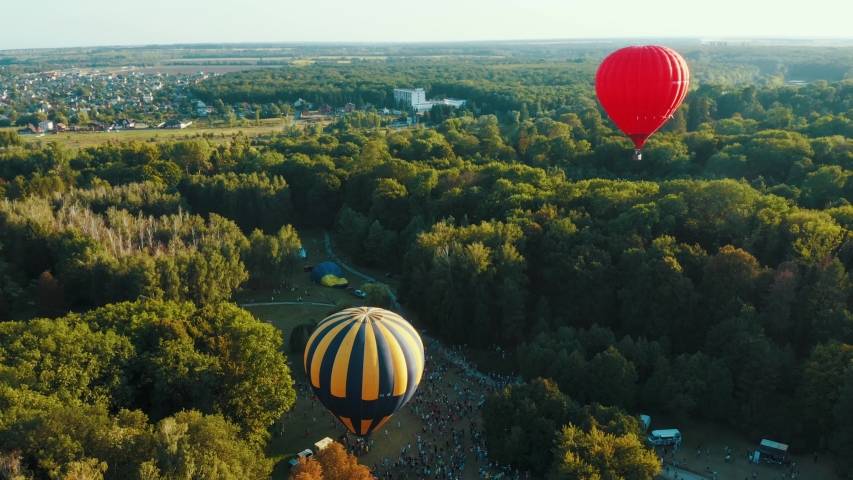Hot air balloons takes off among the trees in the park at the sunset. Aerial footage 4k