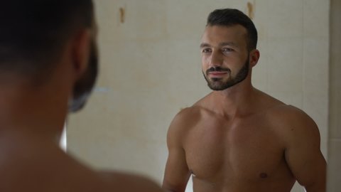 Sexy smiling man spraying perfume on body bathroom, preparing for romantic date