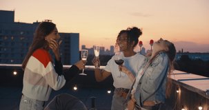 Outdoor shot of young people toasting drinks at rooftop sunset party. Young girl friends hanging out with drinks, talking, chatting , celebrating birthday. 4k slow motion raw video footage 60 fps