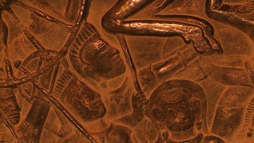 A steady, close up shot of beautiful engravings of faces on a wall.