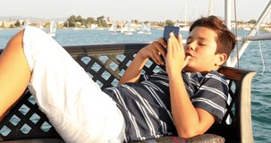 Portrait of a caucasian teenager traveling by yacht and playing video game with smartphone at sunny summer vacation day