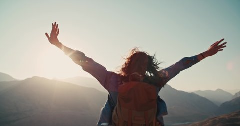 Young girl standing on top of mountain and victoriously raising hands up, looking far away - zennism, freedom, adventure concept 4k footage