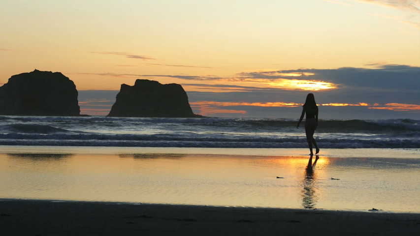 A cute 13 year old Asian teenage girl enjoys watching a stunning summer sunset at Rockaway Beach on the Oregon Coast.