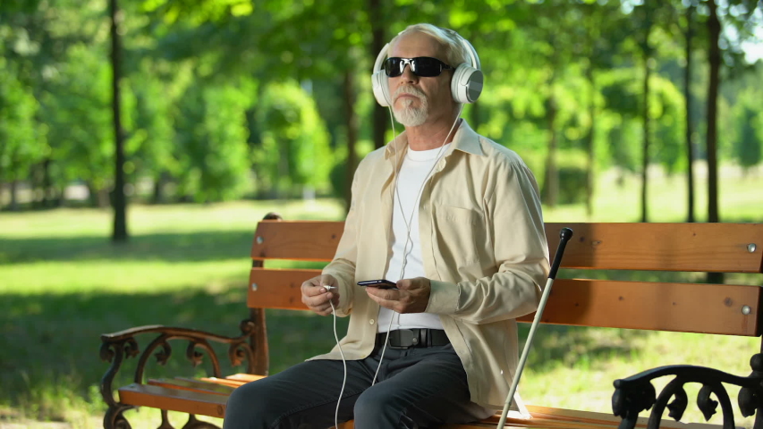 Old blind man putting headset cable in phone, listening voice message, audiobook