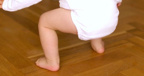 Little feet walking on floor. Close up of baby learning walk. Mmther helping infant going. Baby first steps. Beautiful baby feet learn to walk. Child steps with father support. Toddler feet
