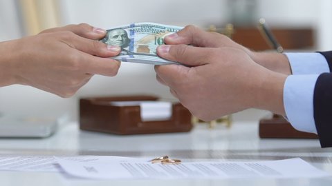 Male and woman pulling dollars, divorce policy and engagement ring on table