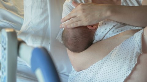 Mother breastfeeds a newborn baby in modern hospital on a hospital cot. Breastfeeding in the first hours after birth, woman caresses newborn baby. Emotional moment in beautiful lighting