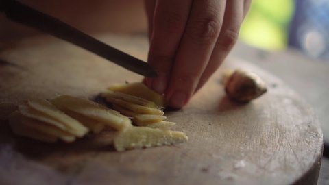 Lady chopping ginger to pieces on wooden board. Slow motion.