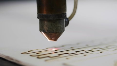 Industrial laser is cutting a pattern on a plywood sheet and moving slowly, close up.