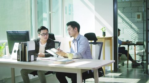 two young asian men entrepreneurs discussing business in office of small company