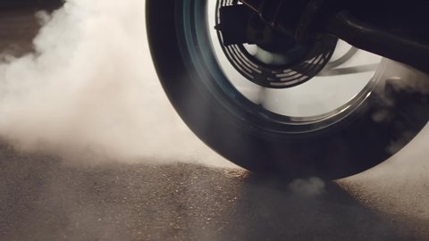 Close up of a motorcycle wheel burning rubber. Smoke and sparks from under the wheels of a sport motobike. Night racing. Need for speed.