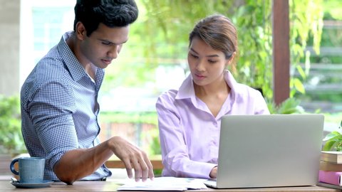 4K Medium shot of asian businessman and businesswoman talking and sharing idea about financial business with using laptop computer and internet at outdoor coffee shop. Outdoor office working concept.