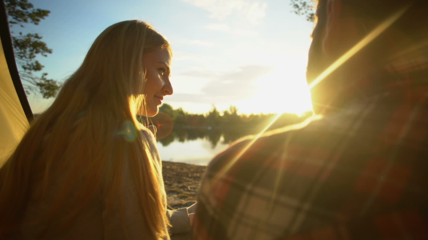 Couple drinking water and watching beautiful sunset in tent, discussing relation
