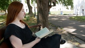 Girl reads a book in a park on a wooden bench