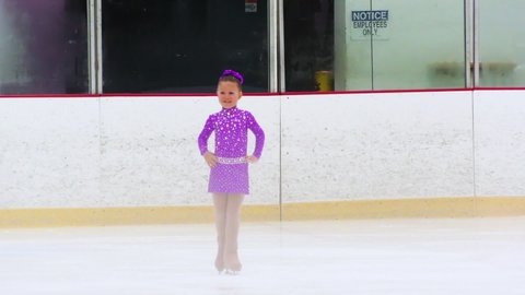 Little figure skater practicing her routine on an indoor ice rink.