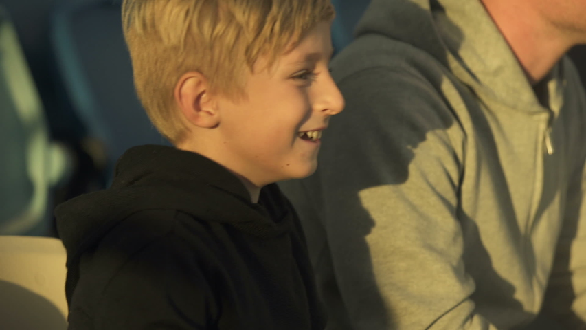 Little boy rejoicing winning score, watching sport game at stadium with father