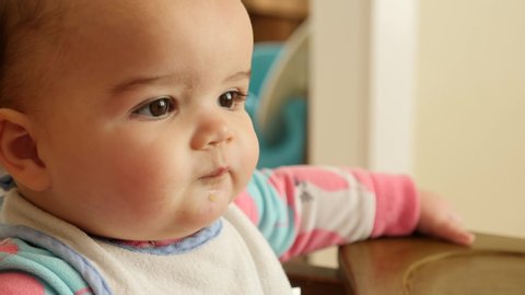An adorable baby girl being fed in her high chair at the kitchen table