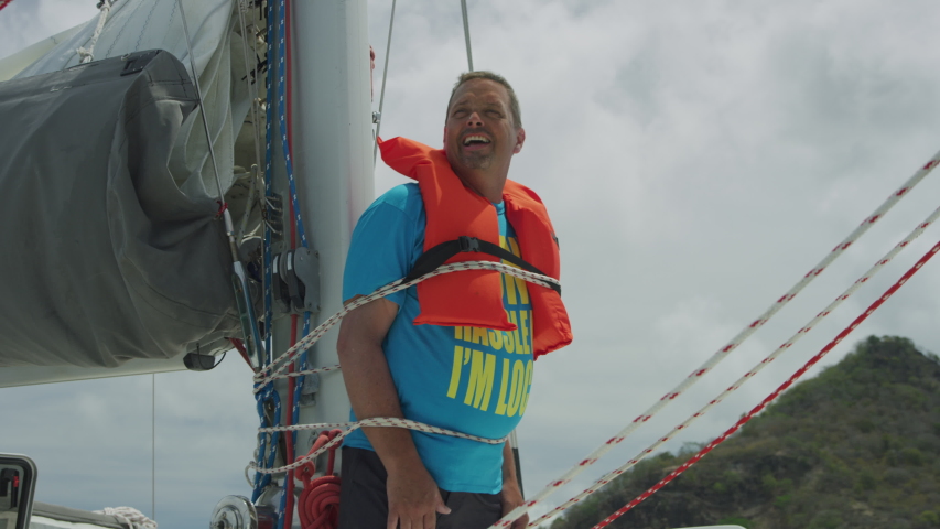 Smiling man yelling while tied to mast of sailboat with rope / Argyle, Carriacou, Grenada