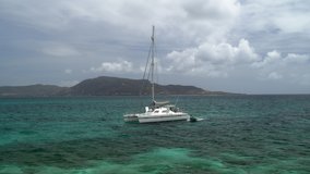 Distant motorboat leaving catamaran in ocean near island / St. Vincent and the Grenadines