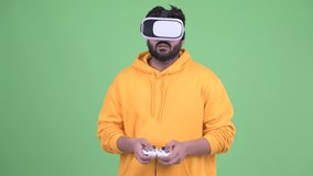 Young overweight bearded Indian man playing games and using virtual reality headset
