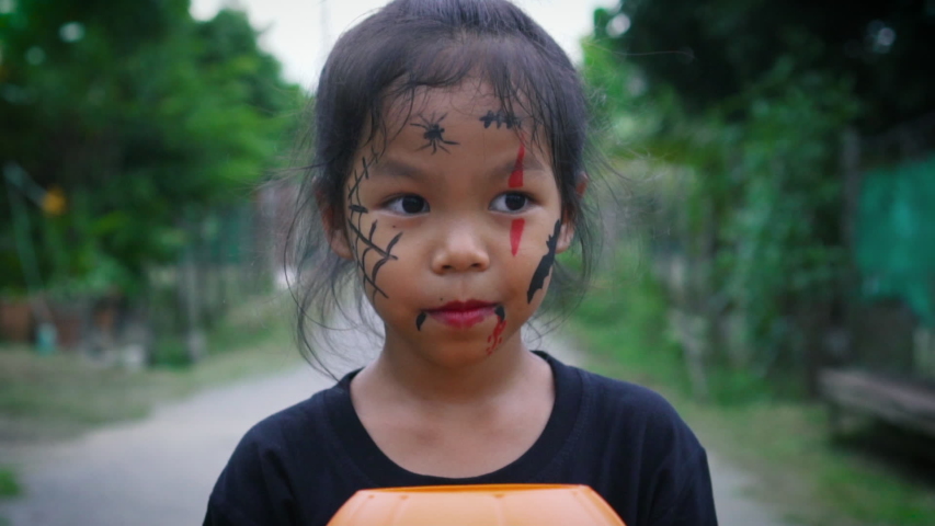 Asian little girl with a painted face is posing facial expression and walking alone in halloween. The children in demon costumes to celebrating halloween. Kids trick or treat. Slow motion.