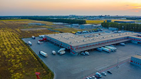 Aerial hyper lapse (hyperlapse - motion time lapse) of the large logistics park with warehouse, loading hub with many semi-trailers trucks standing at the ramps for load/unload goods at sunset