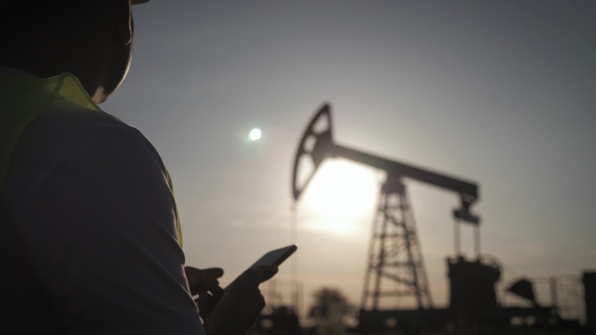 Silhouette of man engineer with phone overseeing the site of crude oil production at sunset.