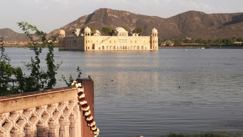 clip of a garland hanging on a wall with jal mahal palace in the background at jaipur, india