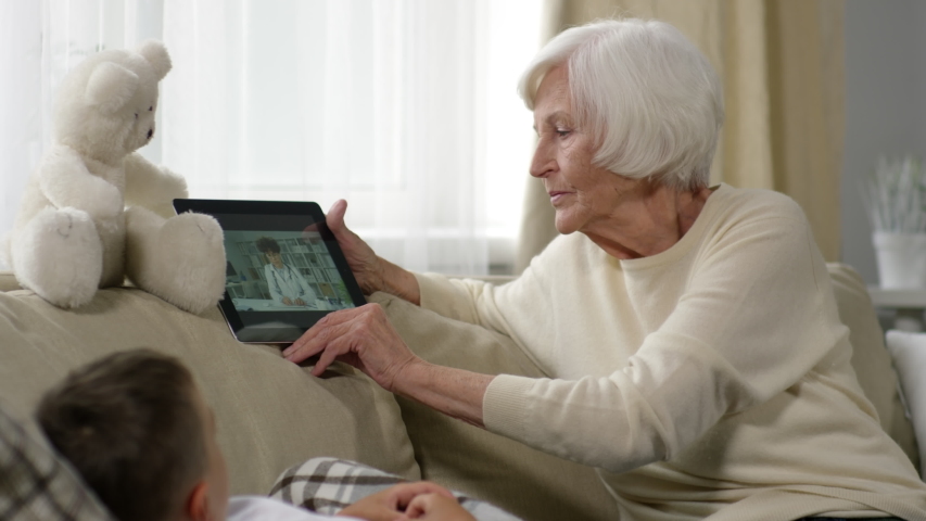 Medium shot of caring grandmother talking to online doctor via video call and describing symptoms of sick grandchild | Shutterstock HD Video #1036400930