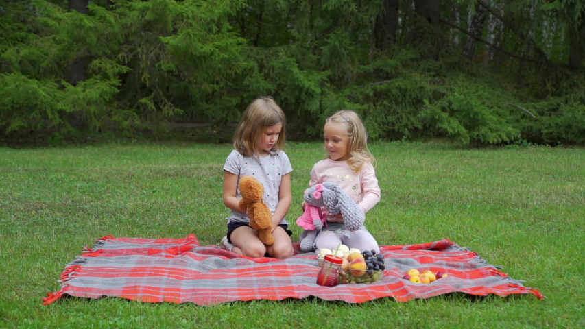 Two Little Girls Playing with Toys while Sitting on the Red Plaid in Summer Park. Friendship, Childhood and People Concept