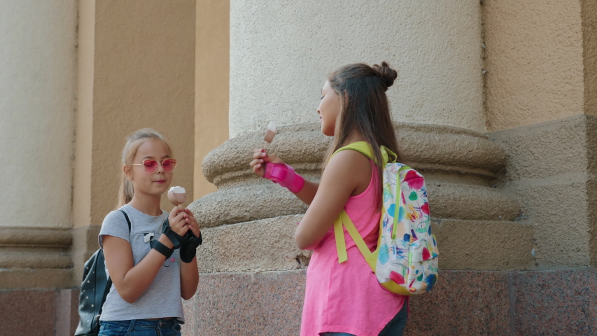 Two girls roller skating eating ice cream and chatting standing near a building in the city. The camera moves in slow motion. Close-up video