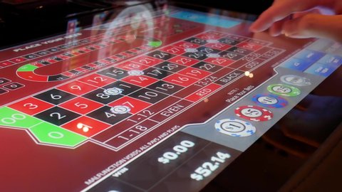 COQUITLAM , British Columbia / Canada - 05 31 2019: Coquitlam, BC, Canada - May 31, 2019 : Motion of people playing casino roulette on machine with reflection spinning ball on screen inside Casino