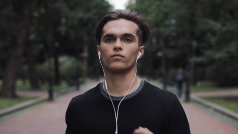 Portrait of Handsome Young Man in Headphones and Smartphone in his Hand Running in Park Close Up Concept Healthy Lifestyle.