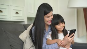 Mother and daughter are play mobile phone together in the living room