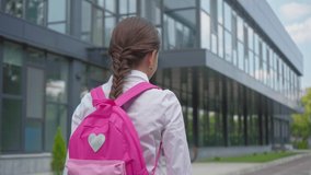 back view of schoolgirl with backpack walking at schoolyard