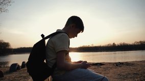 Teen traveler in the open air at sunset sitting with a smartphone. Communication in social networks, shopping in the online store. The concept of modern technology.