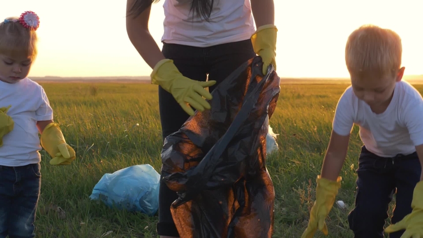 Teamwork. A happy family helps to keep nature clean and collects trash from the green field at sunset. The concept of garbage collection. Volunteers save the world from environmental disaster.