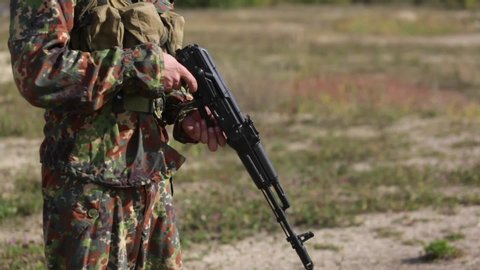 A man in camouflage prepares weapon for shooting. Opens butt, charges a magazine with bullets into Kalashnikov rifle and distort the shutter. AK47 loading Close-up. Soldier hand charging machine gun