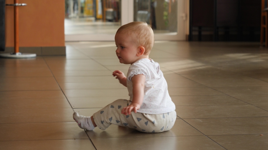 Toddler baby girl sit on the tile floor of food court interior public place