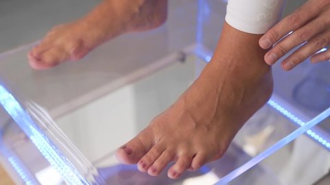 Close-up shot of lady feet on a glass surface while a podiatric physician foot doctor examining her feet