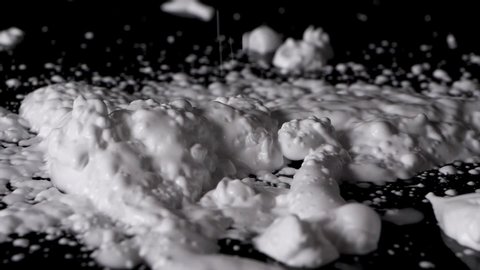 Shaving cream foam being poured from above onto a black bench and background in slow motion.